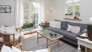 A living room with a grey sofa, wicker chairs, a glass coffee table, and a white console table with a lamp. - 6 Person Holiday Home in Blokhus-by Traum (Blokhus)