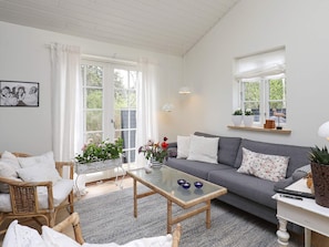 En stue med en grå sofa, fletstole, et glasbord og et hvidt konsolbord med en lampe.