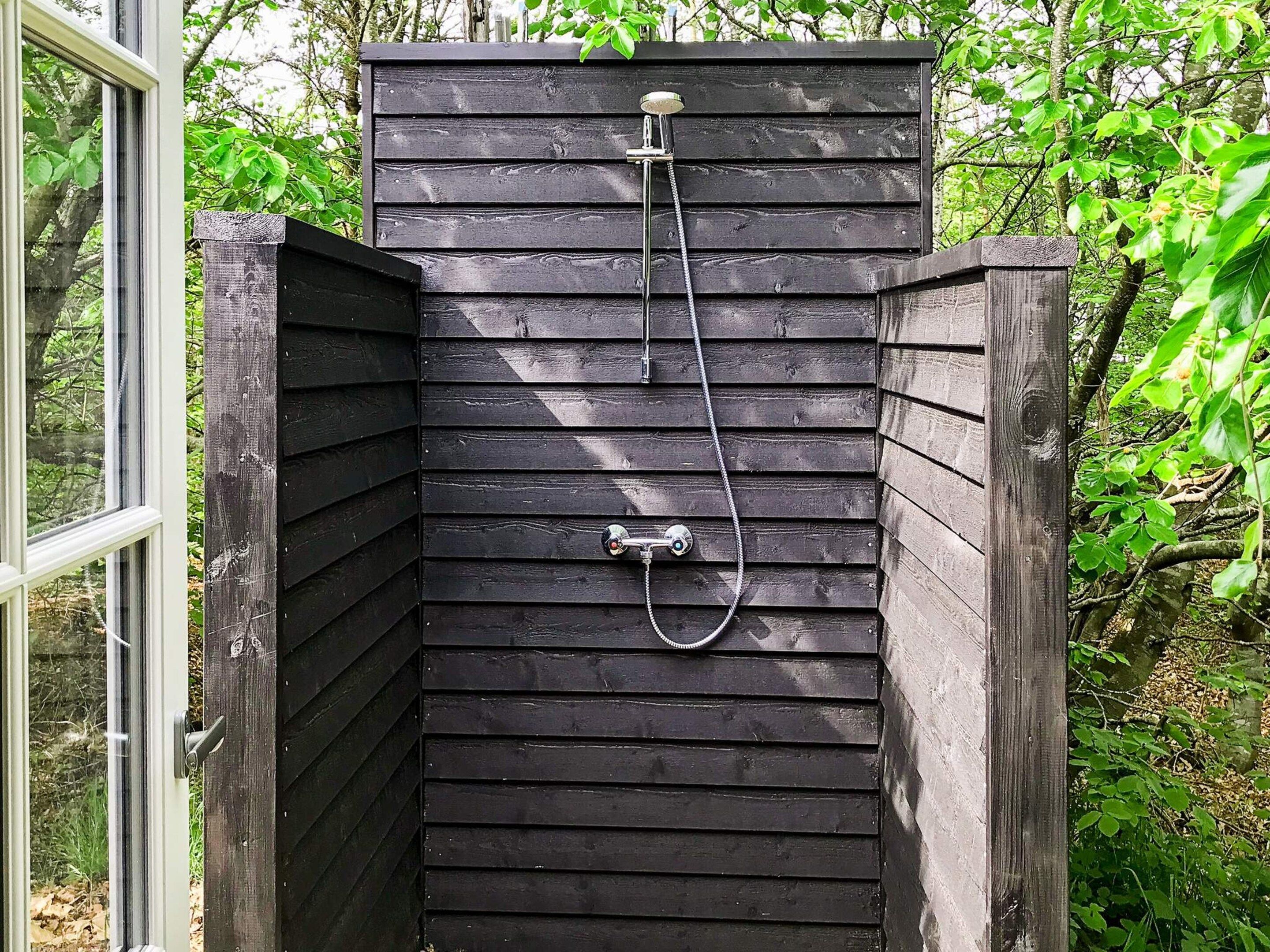 Un recinto de ducha exterior de madera con una manguera y un cabezal de ducha manual.