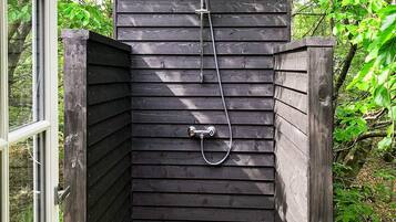 Un recinto de ducha exterior de madera con una manguera y un cabezal de ducha manual.