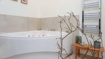 Un baño moderno con una bañera independiente, una mesita de madera con un florero y un perchero para toallas.