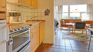 Une cuisine compacte équipée d’une cuisinière, d’un four à micro-ondes et d’une machine à café. À côté se trouve un espace salon avec un canapé, une table basse et une vue sur l’extérieur.