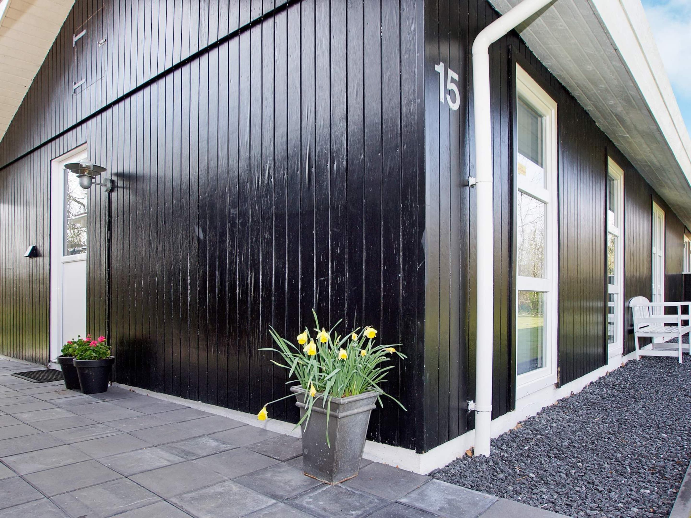 Un bâtiment noir avec une porte et des fenêtres blanches, portant le numéro 15, et une plante en pot devant l’entrée.