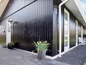 A black building with a white door and windows, number 15, with a potted plant in front.