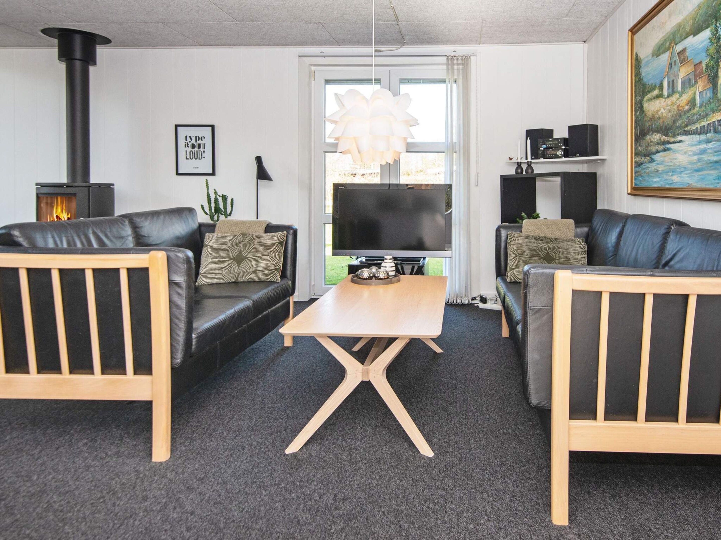 Un salon chaleureux avec deux canapés en cuir noir, une table basse en bois, une cheminée et un téléviseur.
