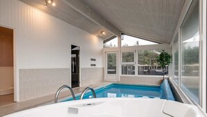 Un espace piscine intérieur moderne, doté d’un jacuzzi, de grandes fenêtres et offrant une vue sur l’extérieur.