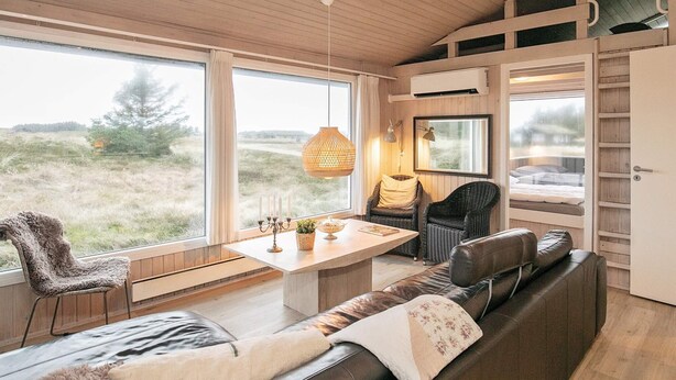 Un intérieur chaleureux avec un plafond en bois, de grandes fenêtres, une table à manger, un canapé et un fauteuil.