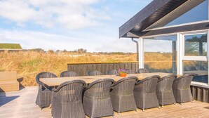 Un espace repas extérieur moderne, doté de mobilier en osier et d’une terrasse en bois, offrant une vue sur un paysage naturel.