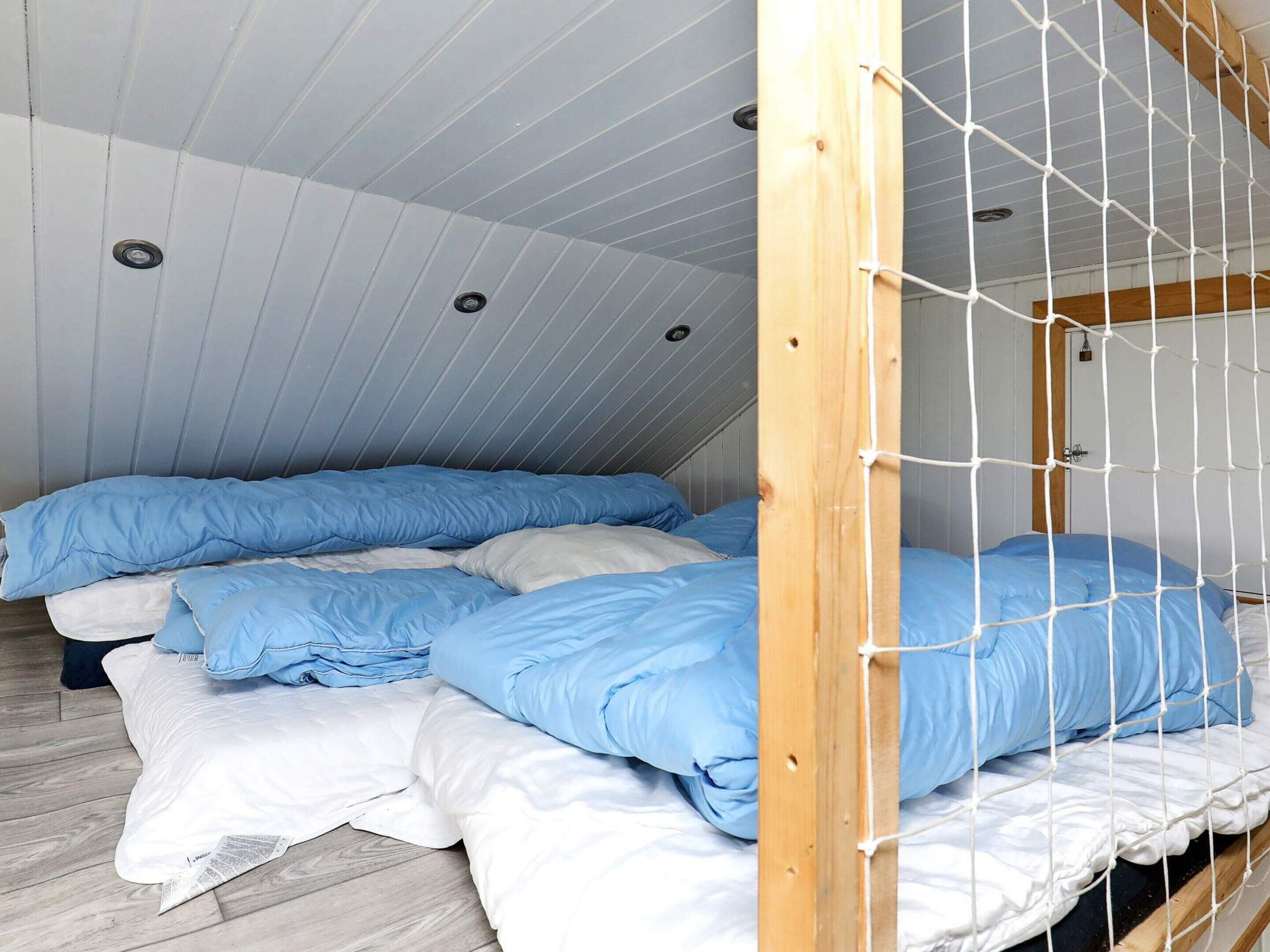 Ein Schlafsaalzimmer mit Etagenbetten, Holzbalkendecke und weißer Wand.
