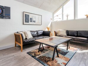 A modern living room with a leather sofa, a wooden coffee table, and a large window providing natural light. - 4 Star Holiday Home in Harboore (Harboore)