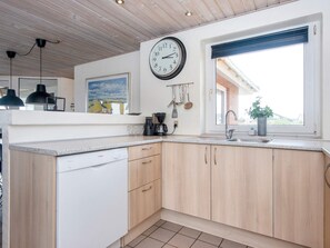 A modern kitchen with wooden cabinets, a Bosch dishwasher, a clock, and a window with a view of a building. - 4 Star Holiday Home in Harboore (Harboore)