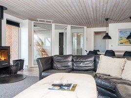 Una sala de estar moderna con chimenea, sofás de cuero, una mesa de centro con revistas, y un comedor con sillas y una mesa.