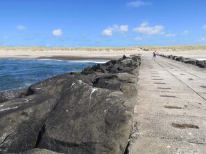 A concrete walkway along a rocky shoreline with waves crashing against the rocks. - 4 Star Holiday Home in Harboore (Harboore)