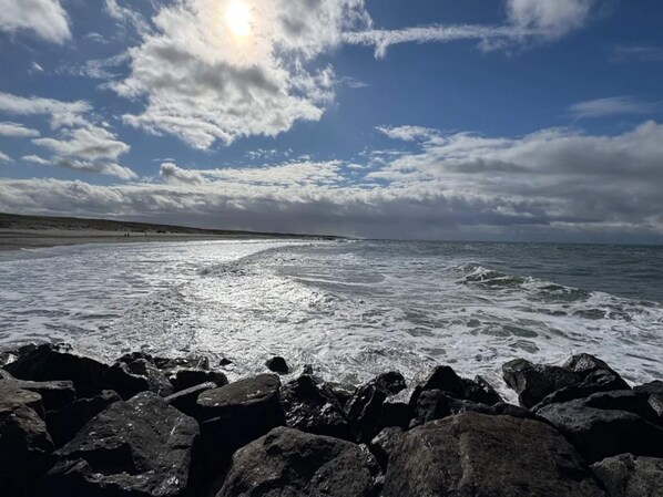 A rocky shoreline with waves, a clear sky, and a distant horizon.