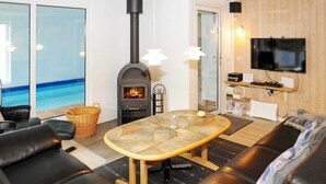 A cozy living room with a fireplace, a television, and a view of a pool. - 4 Star Holiday Home in Norre Nebel (Norre Nebel)