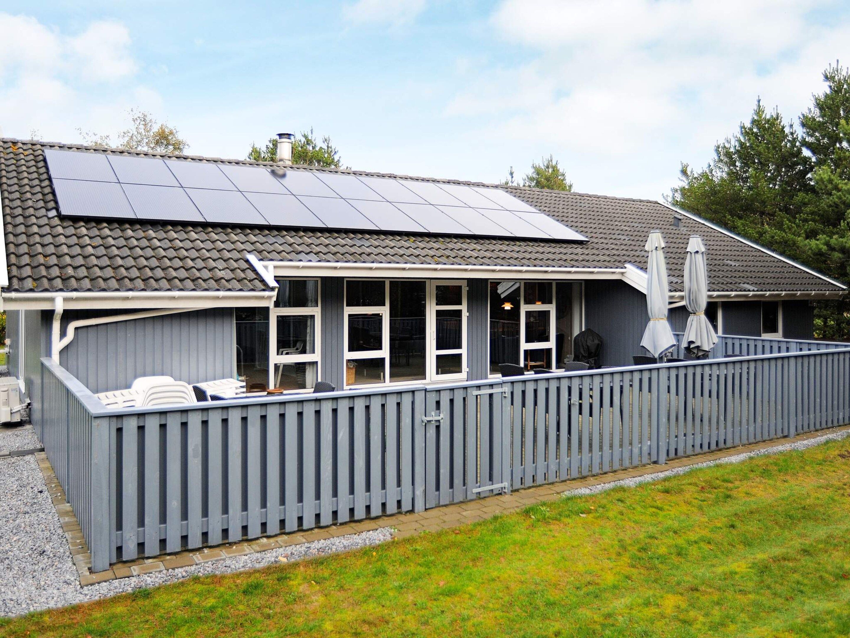 Ein Haus mit überdachter Terrasse, Solaranlage und einem umzäunten Außenbereich.