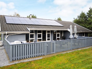 Et hus med en overdækket terrasse, solpaneler og et indhegnet udendørsområde.
