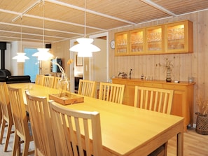 Un espace repas comprenant une table et des chaises en bois, des luminaires suspendus et un meuble contenant de la verrerie.