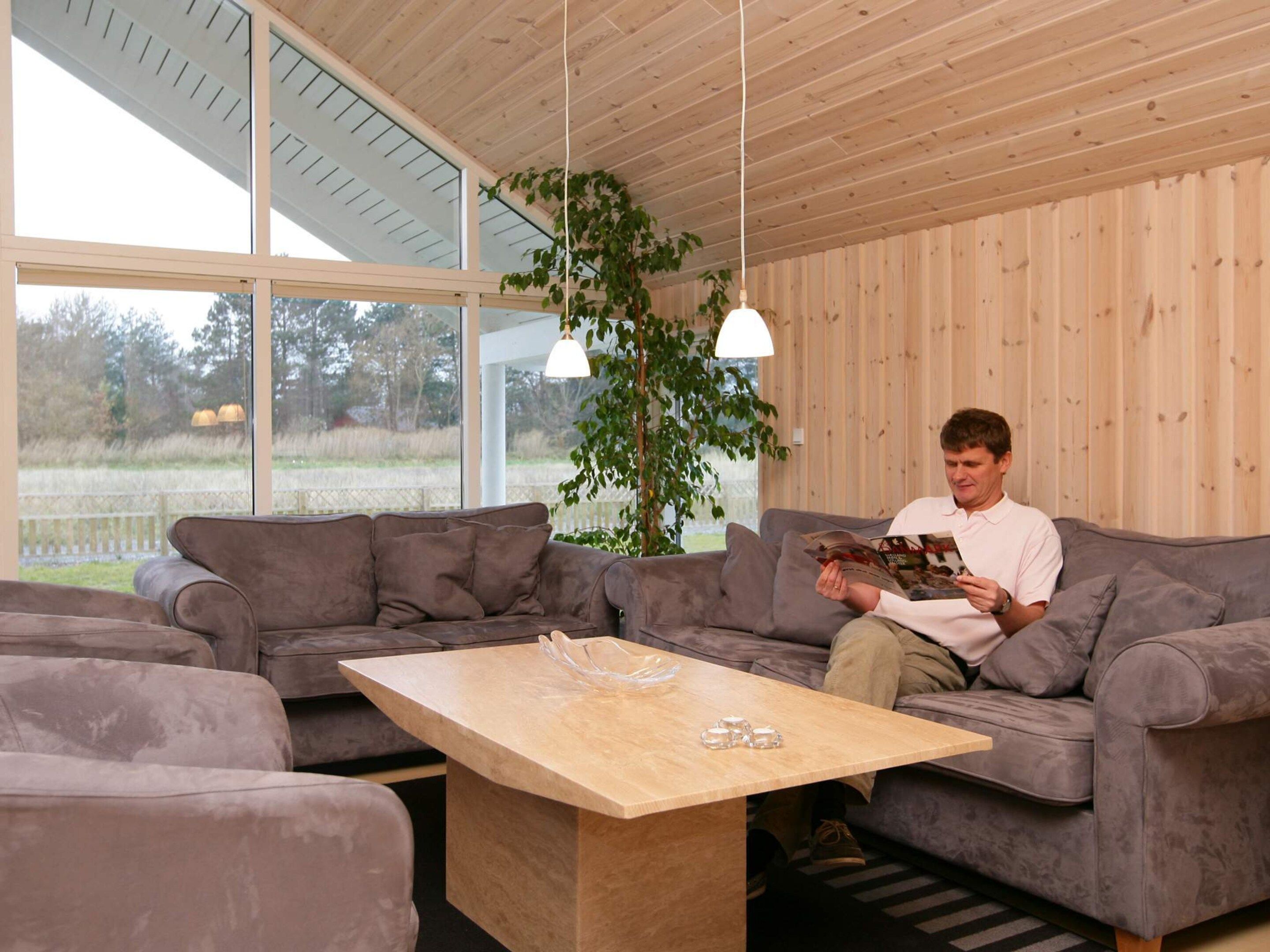 Ein modernes Wohnzimmer mit einem grauen Sofa, einem Holztisch und einem großen Fenster mit Blick ins Freie.