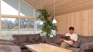 A modern living room with a grey sofa, a wooden coffee table, and a large window offering a view of the outdoors.