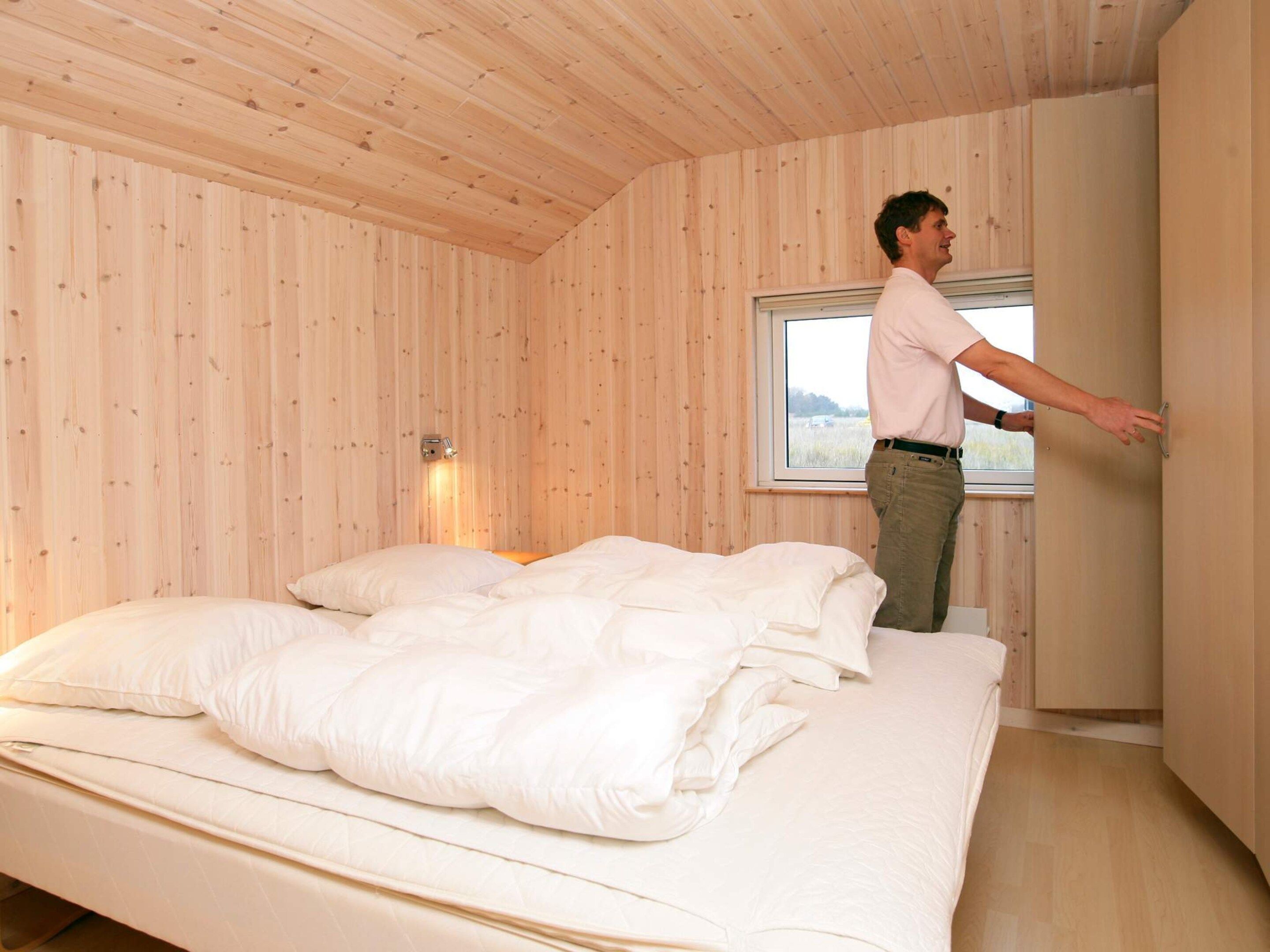 Een kamer met een bed, een raam en een wandlamp.