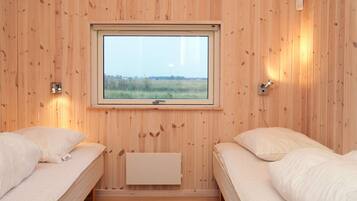 A room with two beds, a window with a view of a field, and a wall-mounted light fixture.