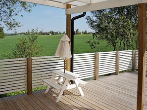 A wooden deck with a white bench and table, a white umbrella, and a view of a green field.