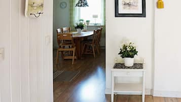 A hallway leading to a dining area with wooden chairs and a table, a white console table with a plant, and a framed artwork on the wall.