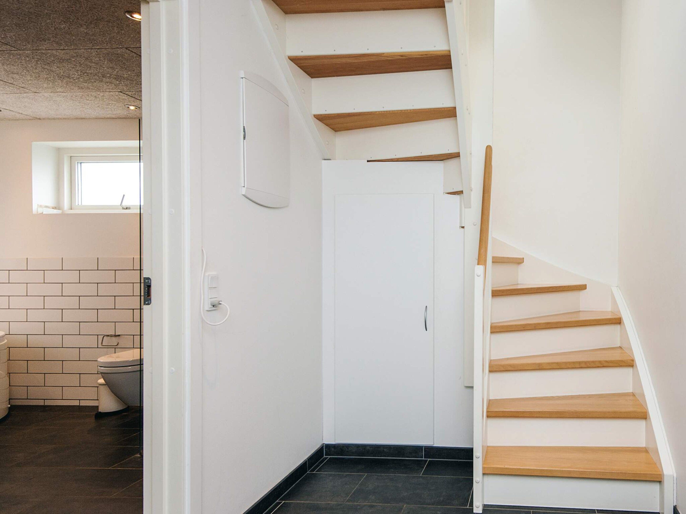 Un interior moderno con una escalera, una puerta blanca y un ventanal visible.