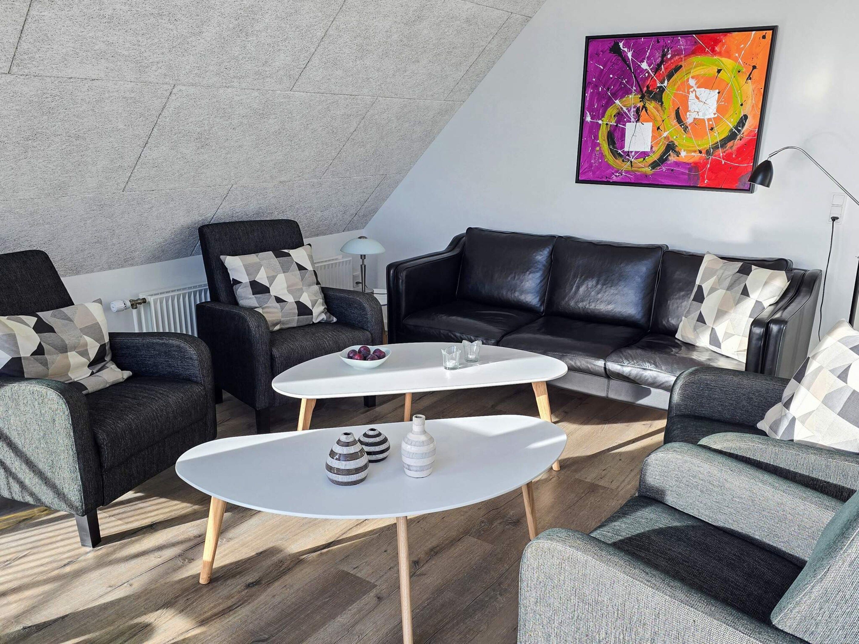 A modern living room with a black leather sofa, a white coffee table, and a geometric patterned armchair.