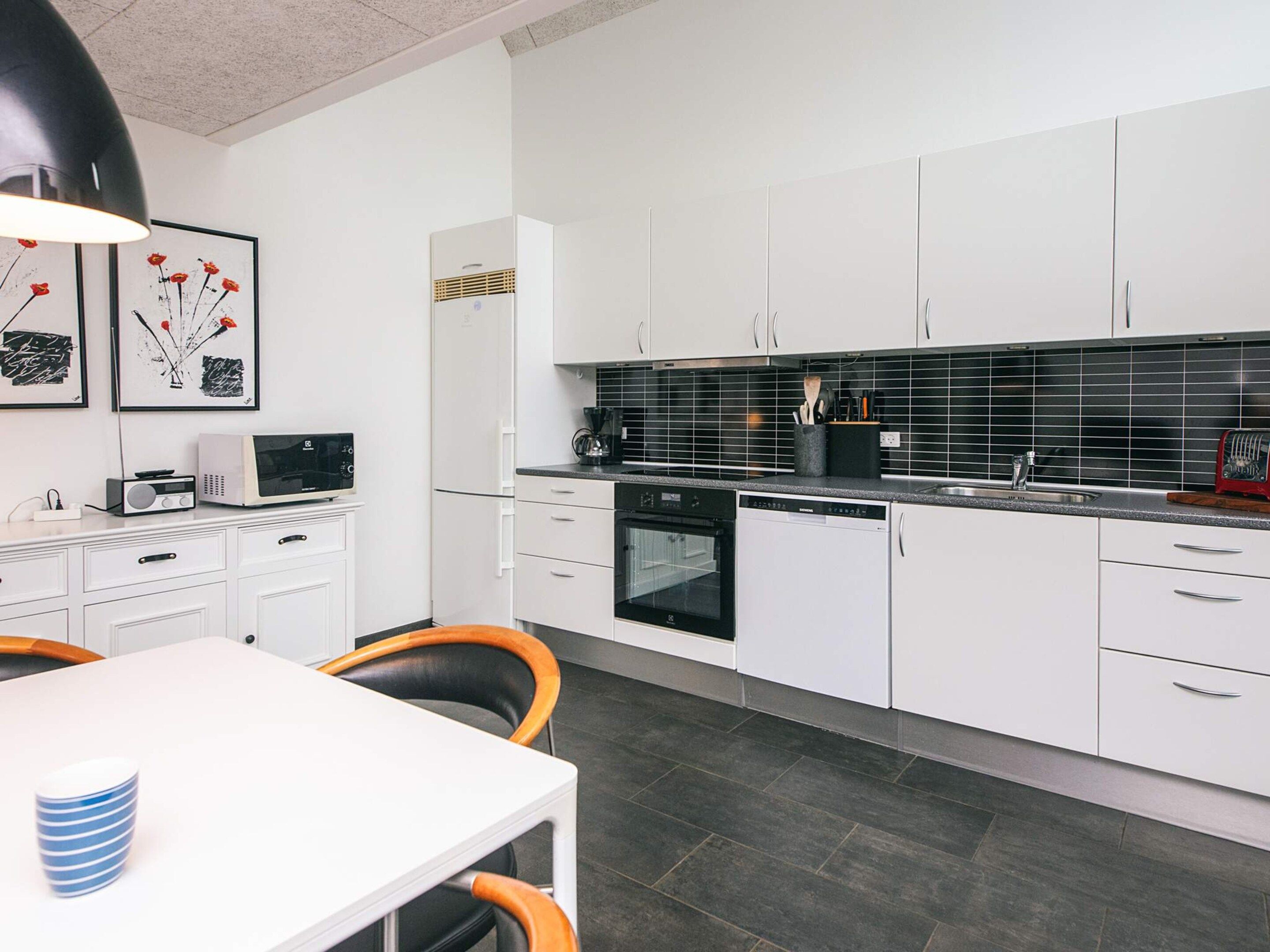A modern kitchen with white cabinets, a black tiled backsplash, and a dining area with a white table and chairs.