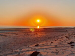A beach at sunset with a clear sky, calm sea, and visible footprints on the sand.
