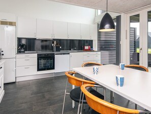 A modern kitchen with white cabinets, a black oven, and a dining area with a white table and wooden chairs. - Comfy Holiday Home in Jutland near Sea (Rømø)