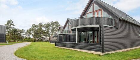 Une maison moderne à deux étages, dotée d’un balcon, d’une allée en gravier et d’une pelouse.