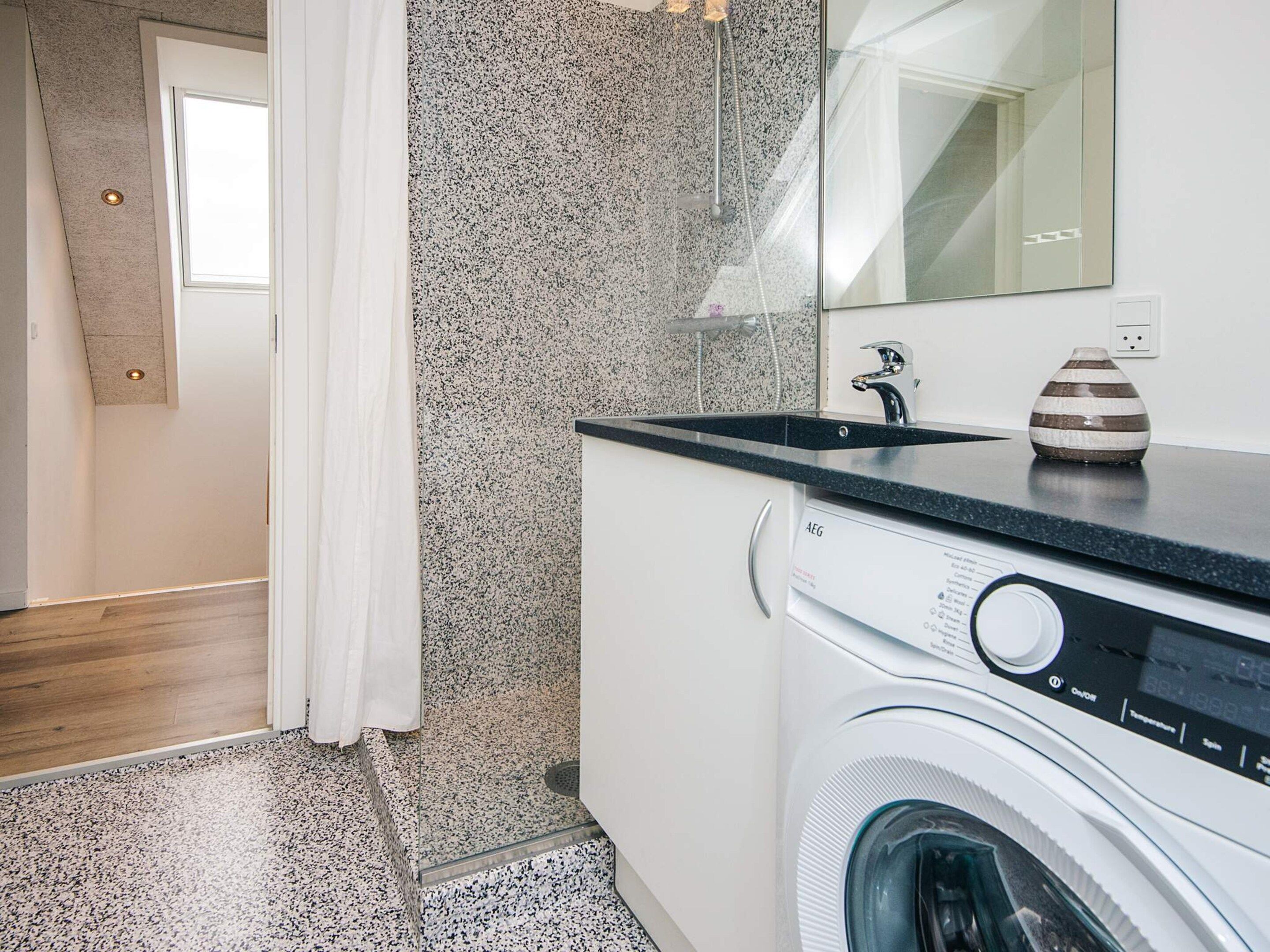 A modern bathroom with a washing machine, a sink, and a shower.