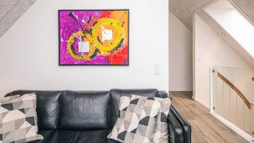 A modern living room with a black leather sofa, geometric patterned cushions, and a vibrant abstract painting on the wall.