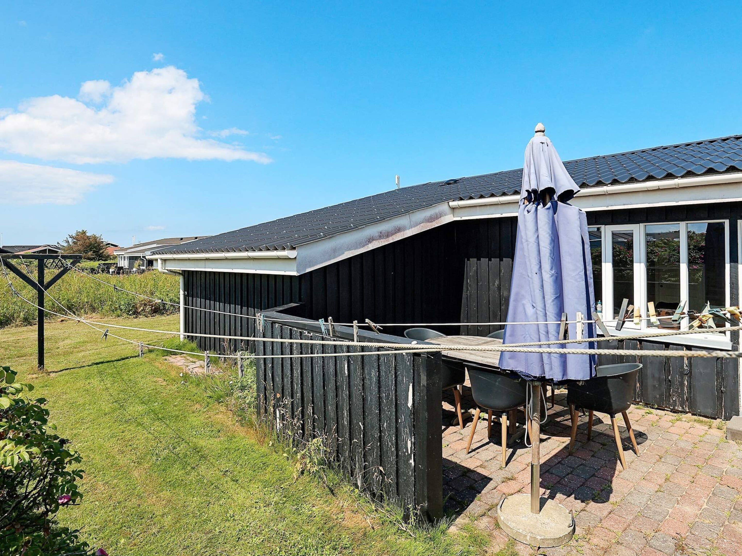 Een overdekt buitengebied met een tafel en stoelen, een houten omheining en een gebouw met een donker dak.