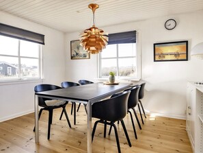 Un coin repas avec une table en bois, des chaises noires, un luminaire suspendu et des œuvres d’art accrochées aux murs.