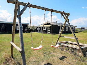 A wooden swing set in a grassy area with a house in the background.
