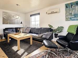 Uma sala de estar moderna com sofá de couro, mesa de centro de madeira, poltrona de couro preta, planta em vaso e um quadro na parede.