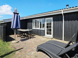 Un espace patio aménagé avec une table et des chaises, un parasol bleu et un fauteuil de relaxation.