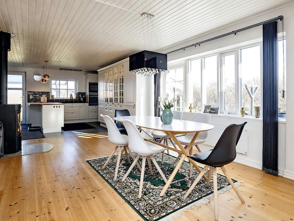A modern kitchen with white cabinets, a dining area with a round table and chairs, and large windows with curtains.