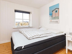 A bedroom with a bed, a window, a wall-mounted lamp, and a poster.