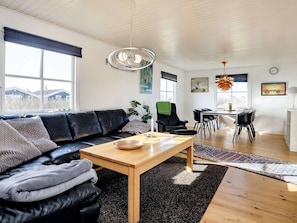 Uma sala de estar moderna com um sofá de couro preto, uma mesa de centro de madeira e uma área de jantar com mesa branca e cadeiras pretas.