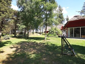 A residential area with a thatched-roof house, a wooden swing set, and a grassy yard with trees. - 4 Star Holiday Home in Blavand (Blavand)