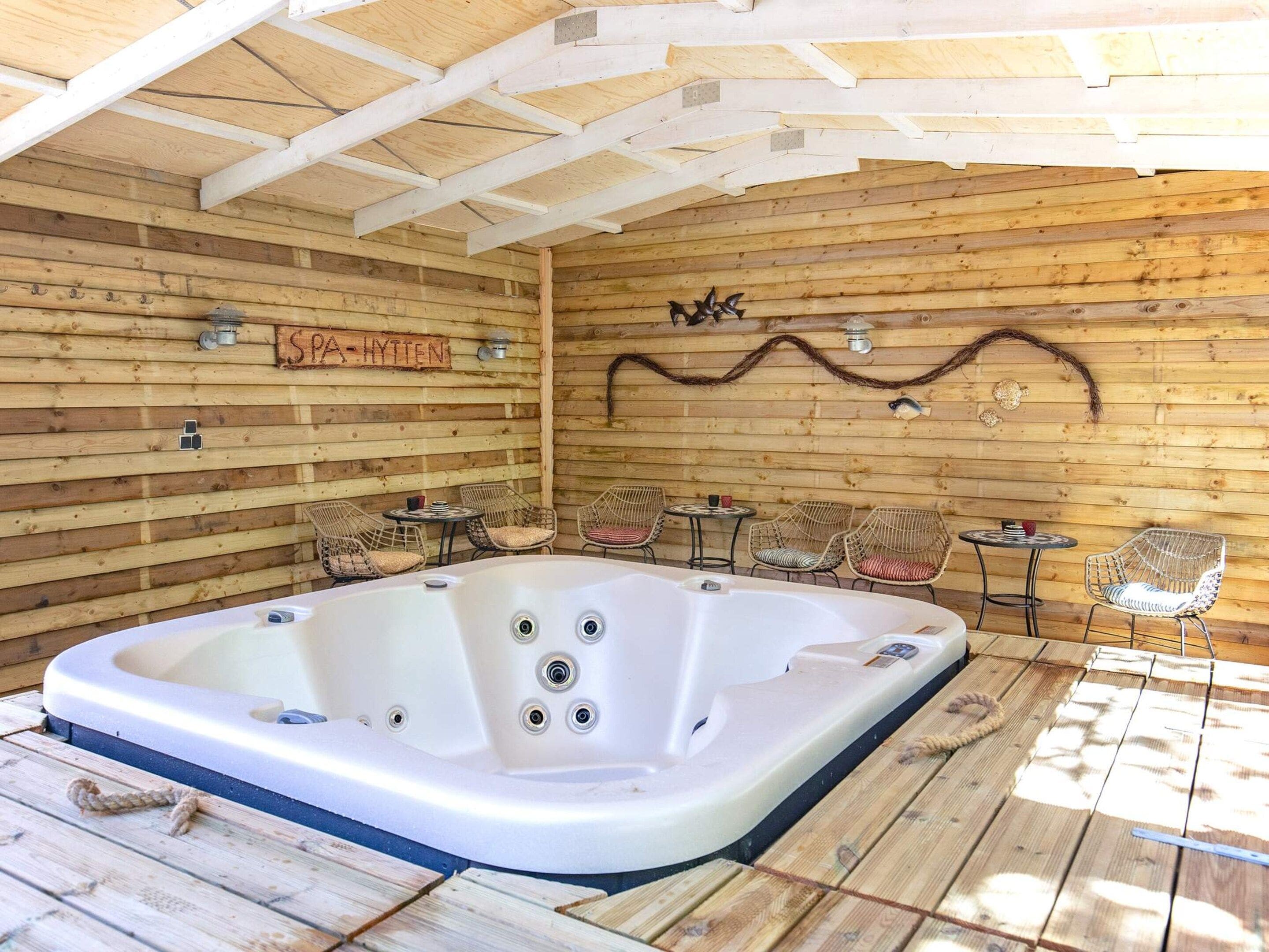 A wooden cabin with a hot tub, wicker chairs, and a sign that reads 'SPA-HYTTEN'.