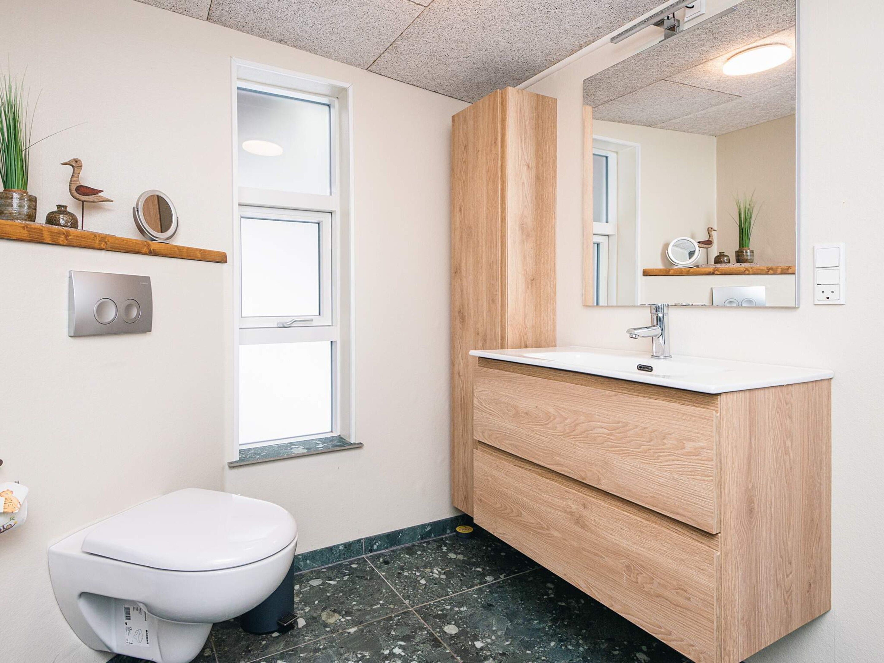 Un baño con inodoro, lavamanos con espejo y ventana.