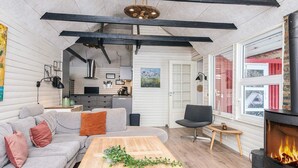 A modern living room with a sofa, coffee table, and fireplace. There is a kitchen in the background with a stove and cabinets. - 4 Star Holiday Home in Blavand (Blavand)