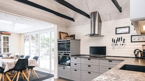 A modern kitchen with a large island, built-in ovens, and a dining area with a view. - 4 Star Holiday Home in Blavand (Blavand)