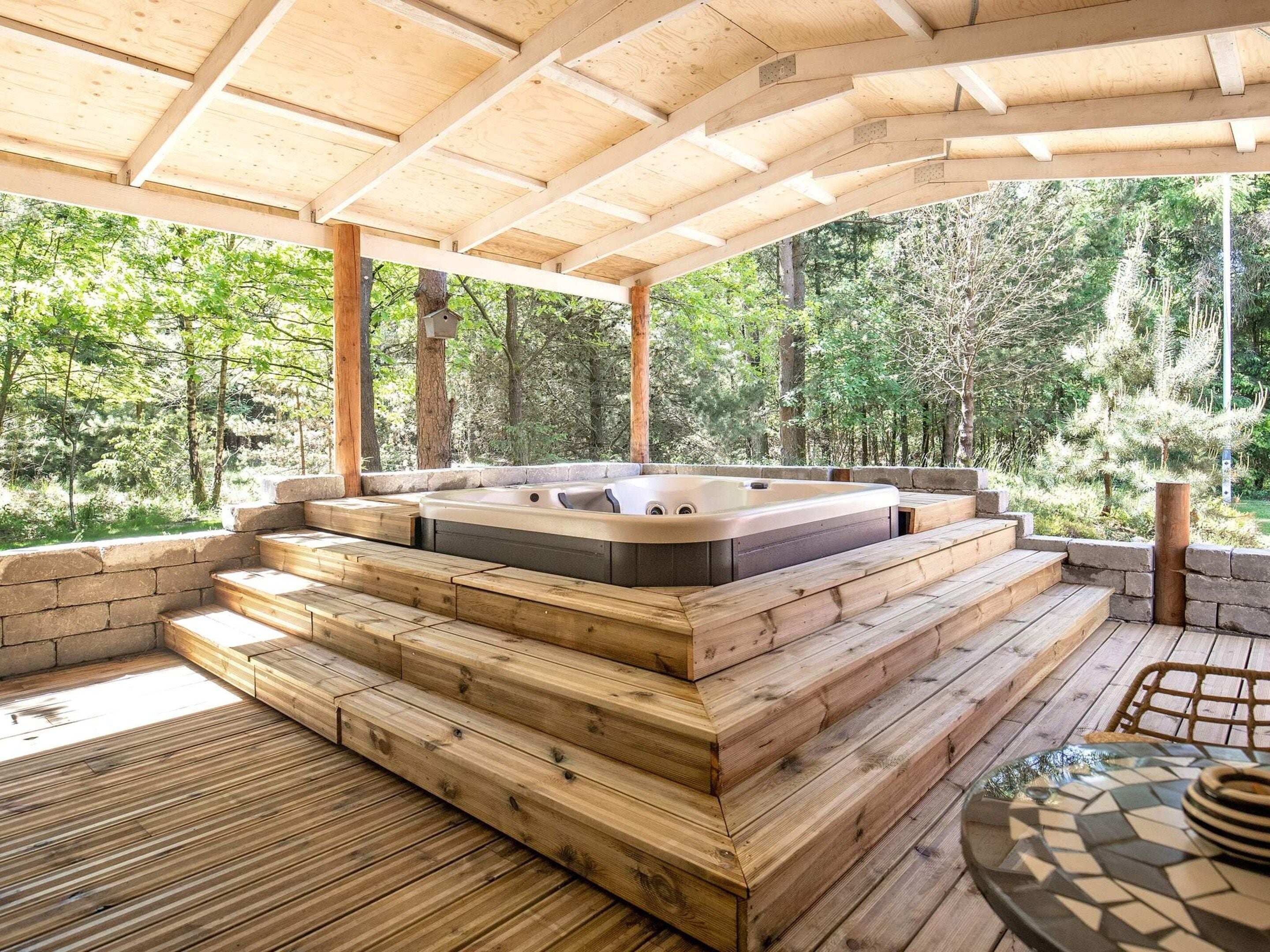 A wooden deck with a hot tub, surrounded by a forest.